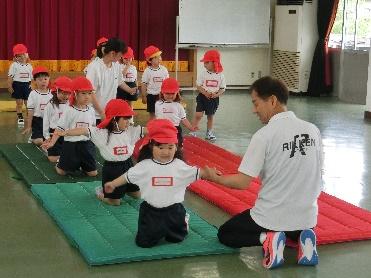 園児がマットの上で体操の先生に教わっている様子の写真