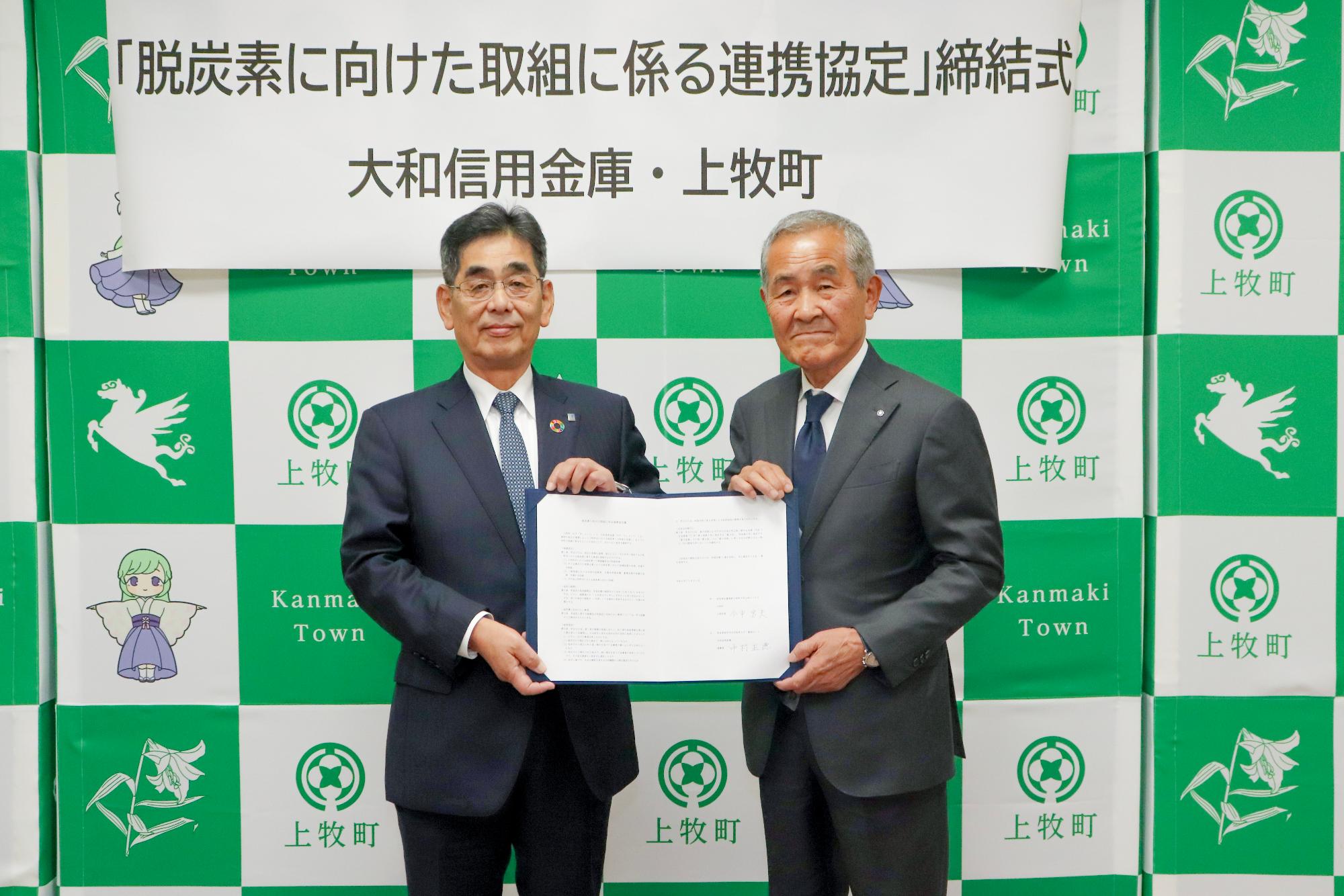 締結式で署名をした締結書を見せる2人
