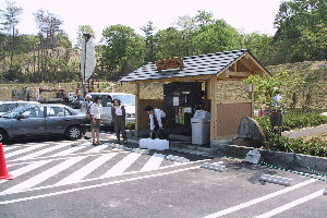 屋根のついた水汲み場にポリタンクをもってきて源泉を組んでいる人の写真