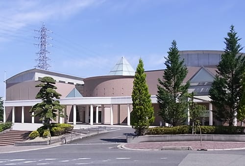 建物前に植木やスロープ、雨除けの屋根付きの通路が整備されている2000年会館の外観写真