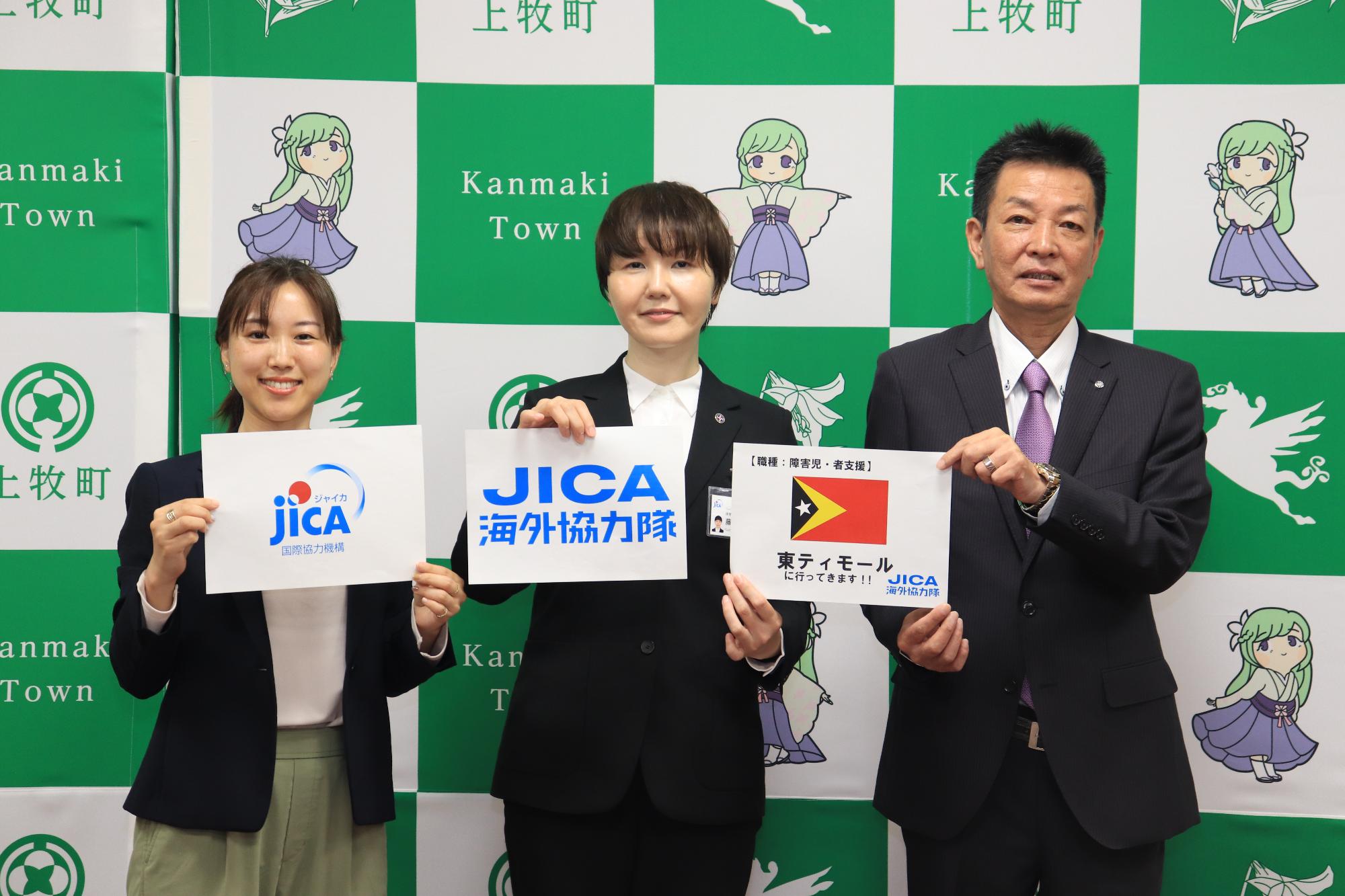 東ティモールの国旗を持って写真を撮るJICA関西国際協力推進員とJICA海外協力隊員と阪本町長の様子