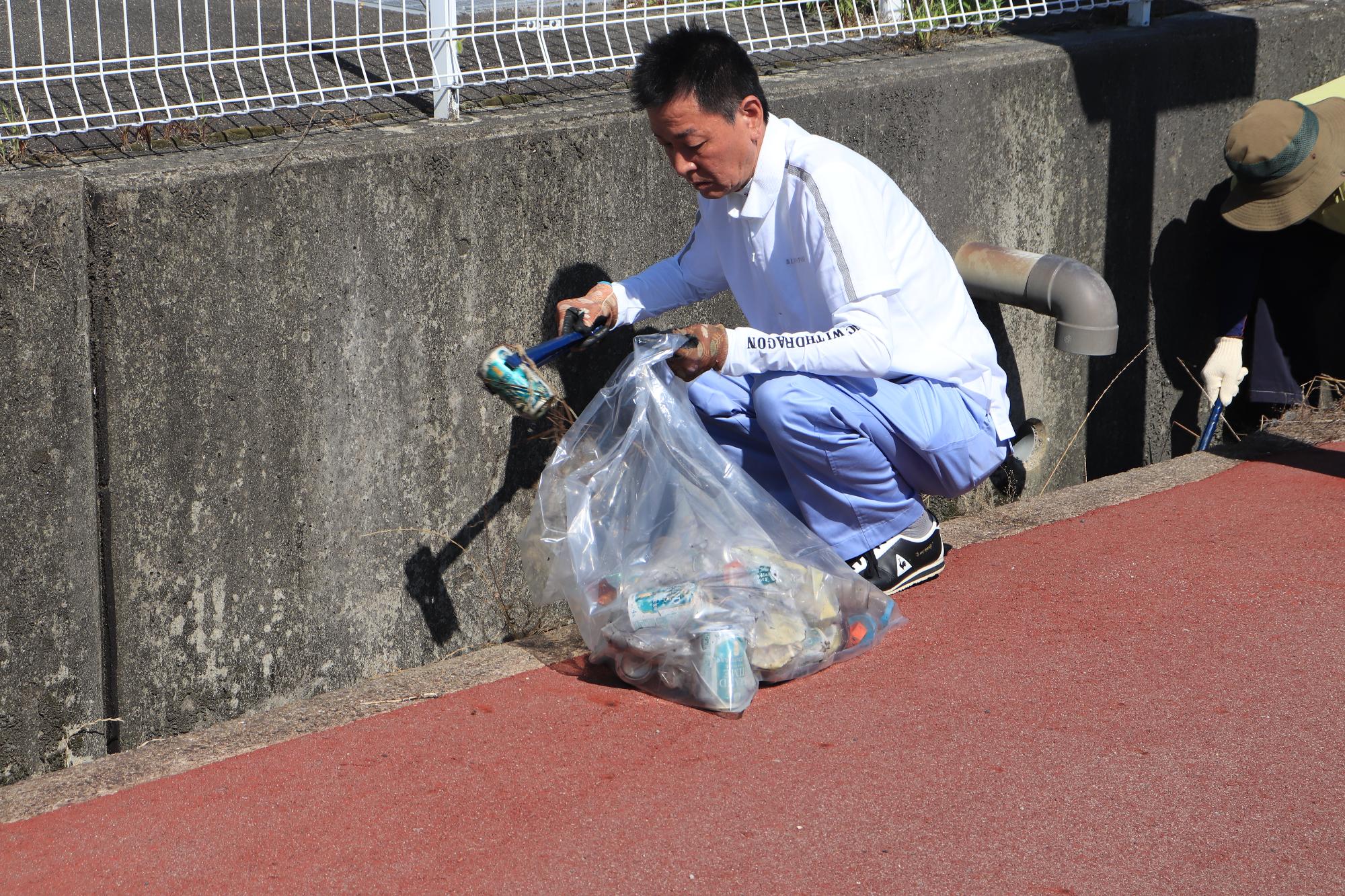 溝に落ちている空き缶を拾う阪本町長