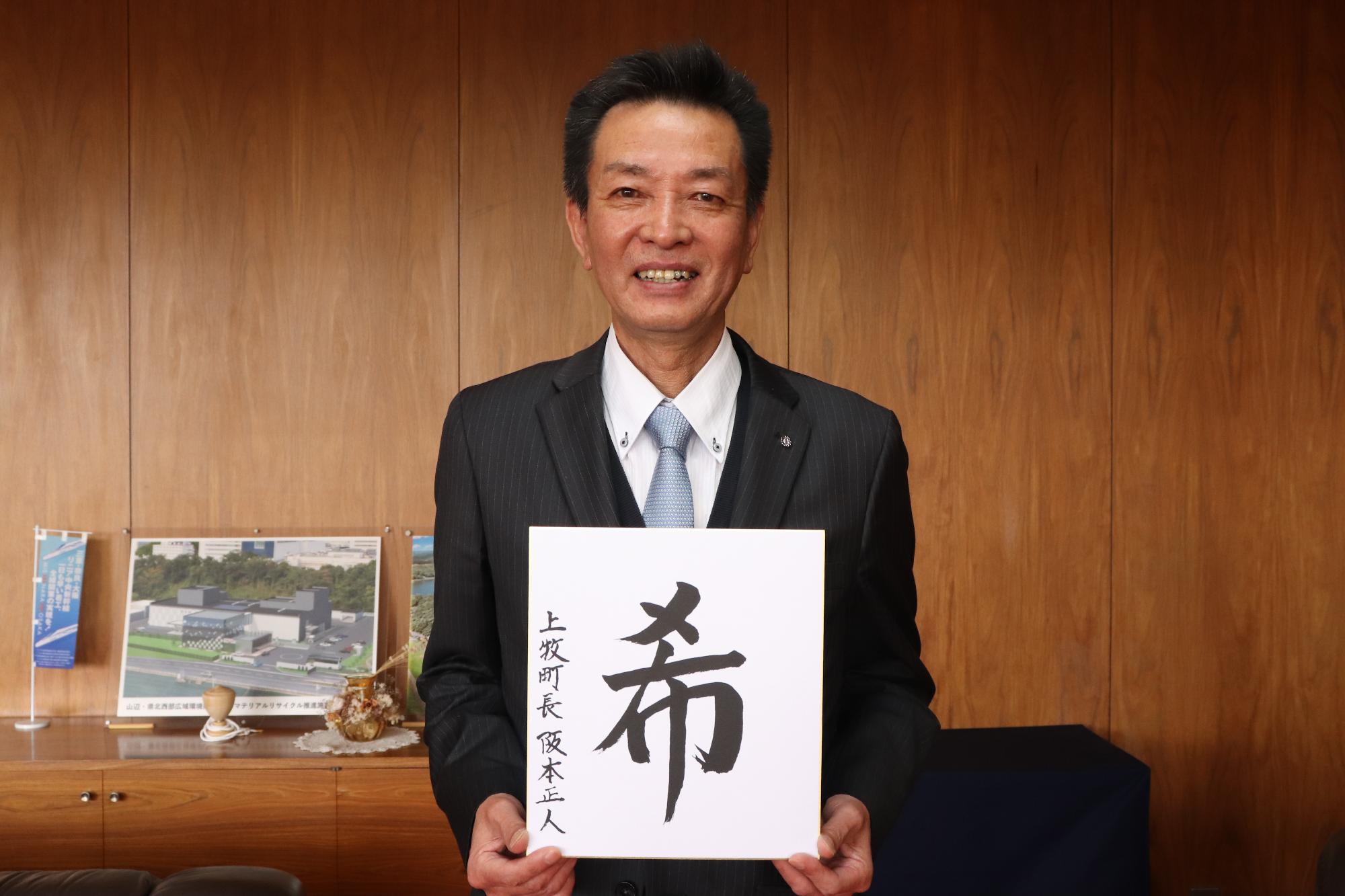 漢字一文字を書いた色紙をもって写真を撮る阪本町長