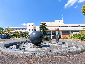 青空のもと、上牧町役場庁舎の外観と庁舎前にある黒い球体状のモニュメントを撮影した写真