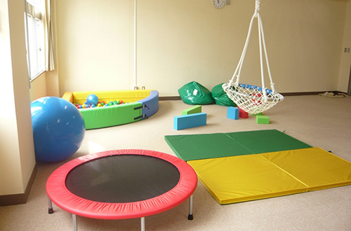 ペガサス教室のプレイルームにトランポリンやマット、バランスボールなどの遊具が置いてある写真