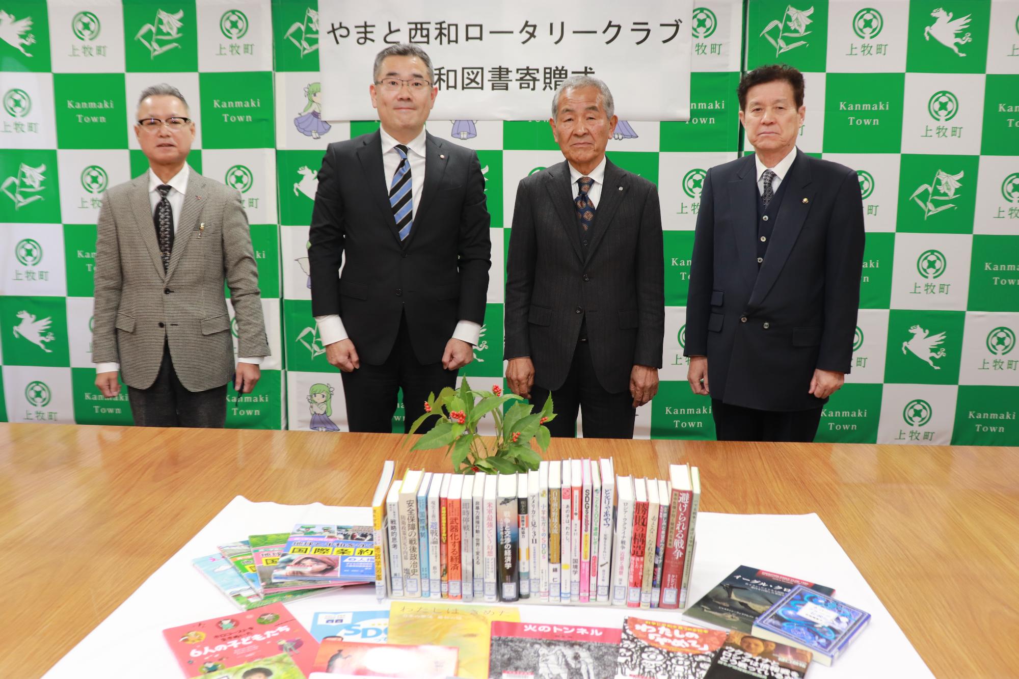 やまと西和ロータリークラブのお2人と今中町長、松浦教育長が並んで立ち、手前の机に寄贈された平和図書が並べられている